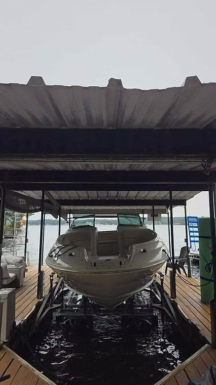 Boat on a lift under a covered dock. Water surrounds the boat. Overcast sky.