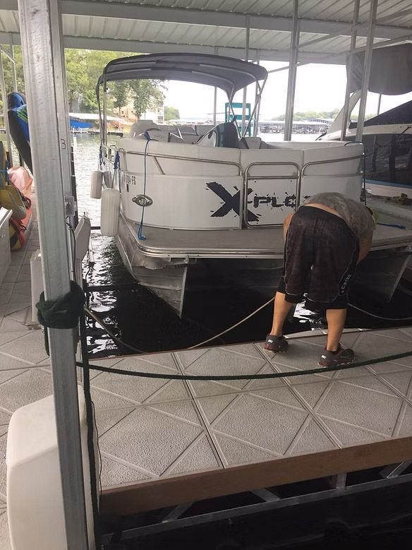 Person at a boat dock, working on a white pontoon boat, near water.