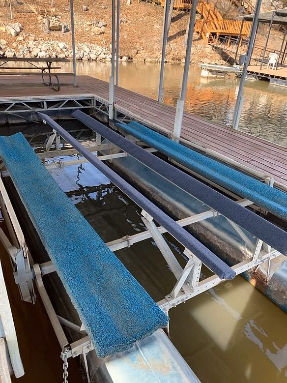 Dock with several boat lifts, featuring blue and gray padded supports, in a lake setting.