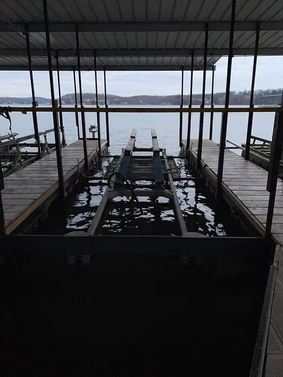 Boat lift structure extending into water under a covered dock on a cloudy day.