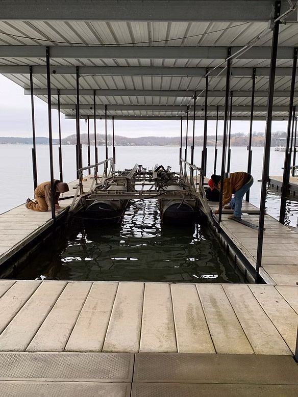 Two people working on a boat lift inside a covered dock on a lake.