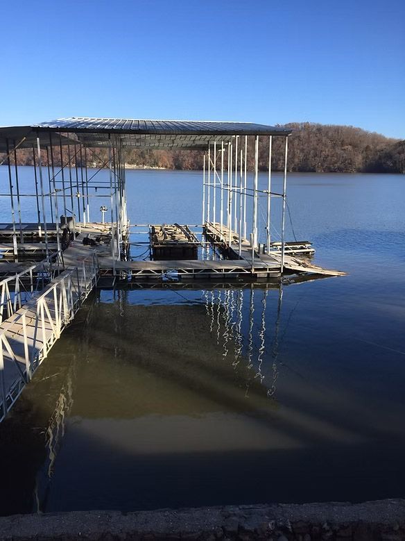 Dock with boat slips on a lake; clear sky, distant hills, and reflections in the water.
