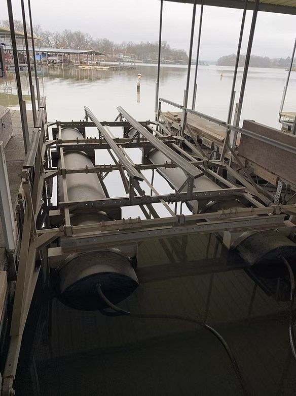 Boat lift in water with a lake in the background, under a covered dock. Overcast day.