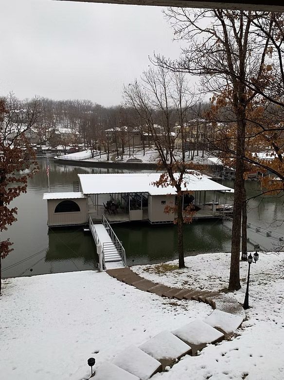 Snowy lake scene with a covered dock and surrounding trees. Gray sky and snow-covered ground.