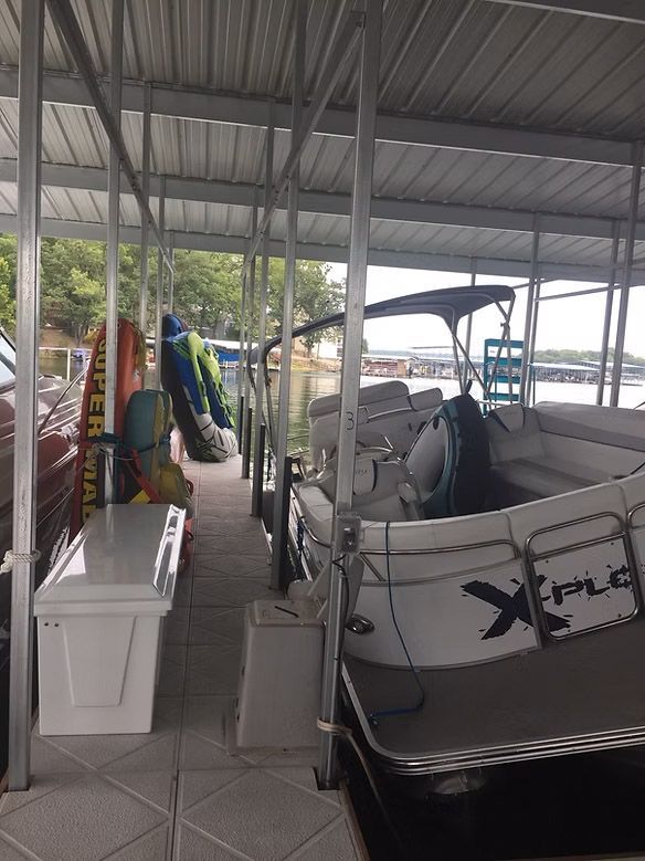 Boat in a covered slip, next to water and docks. Water sports equipment stacked.