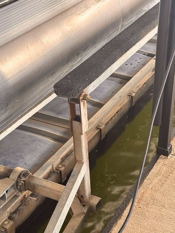 Close-up of a conveyor belt system with a dark, textured surface, next to a water-filled trough.
