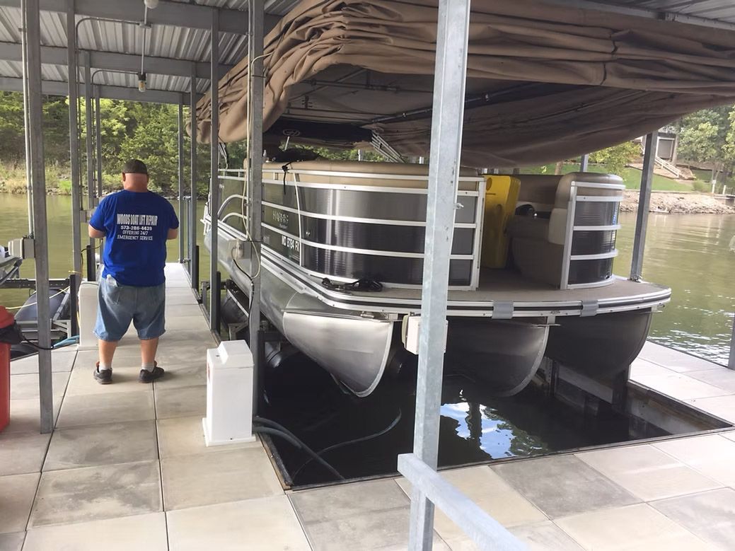 Man stands by pontoon boat in a covered dock. Boat is black and silver.