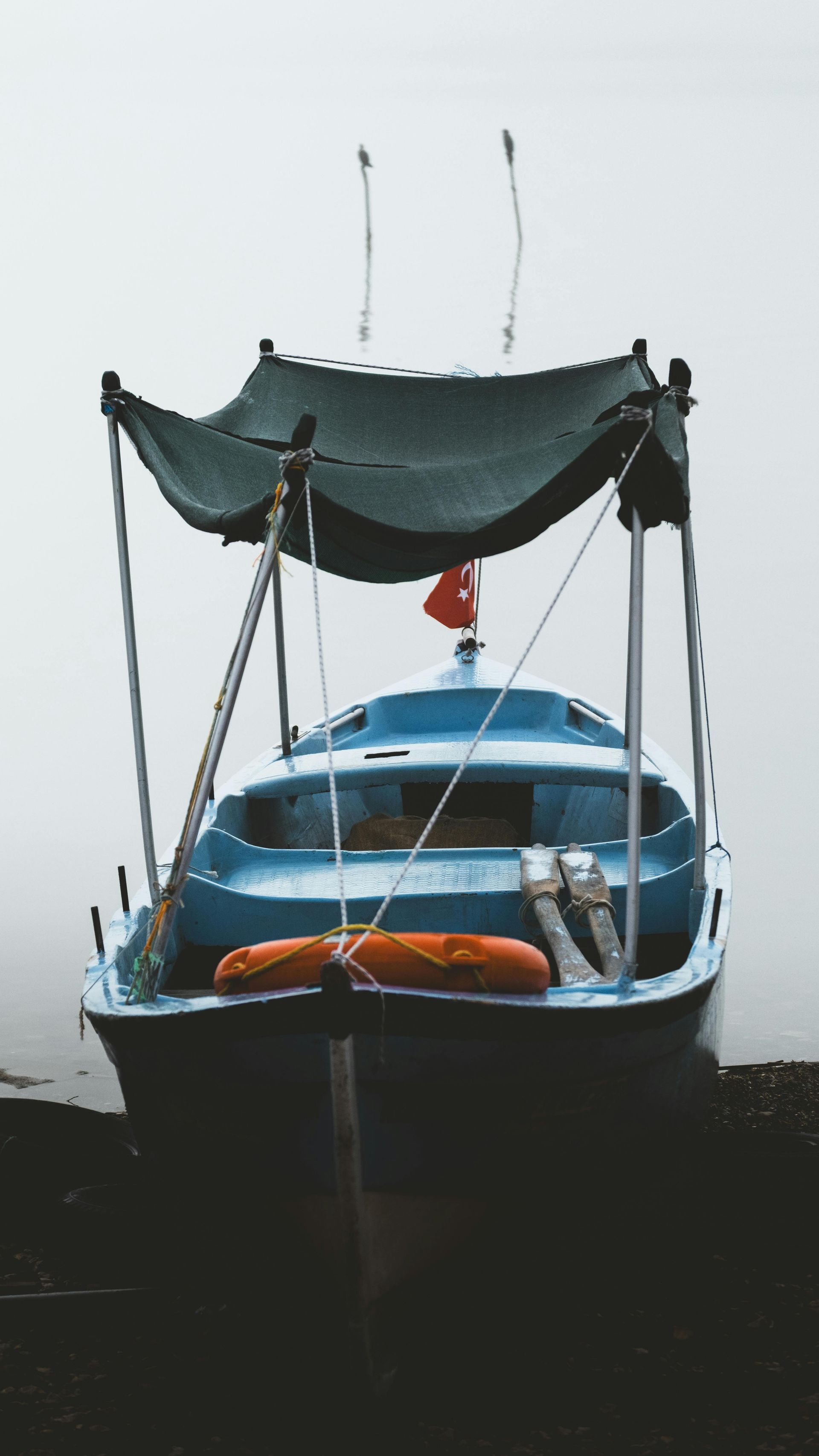 Blue boat with a canopy and Turkish flag, resting on the shore, against a foggy backdrop.