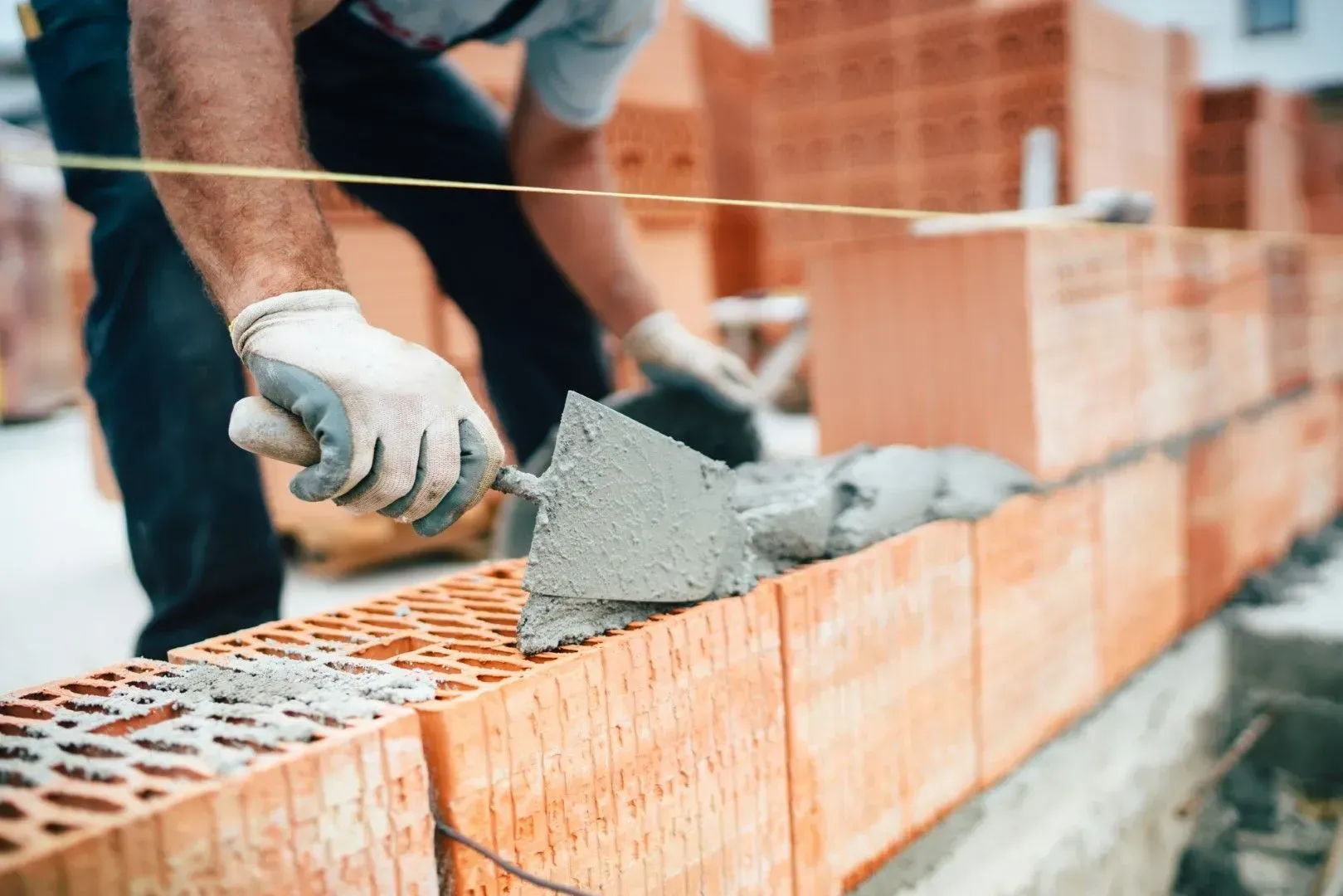 Construction worker laying mortar on a brick wall with a trowel, close-up