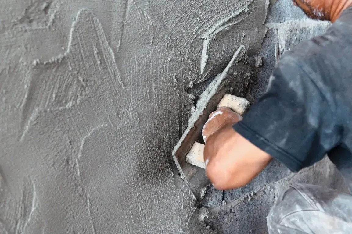 Worker smoothing wet gray plaster on a wall with a trowel