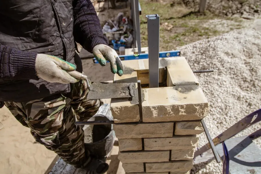 Worker laying bricks for a brick pillar outdoors using a trowel and level