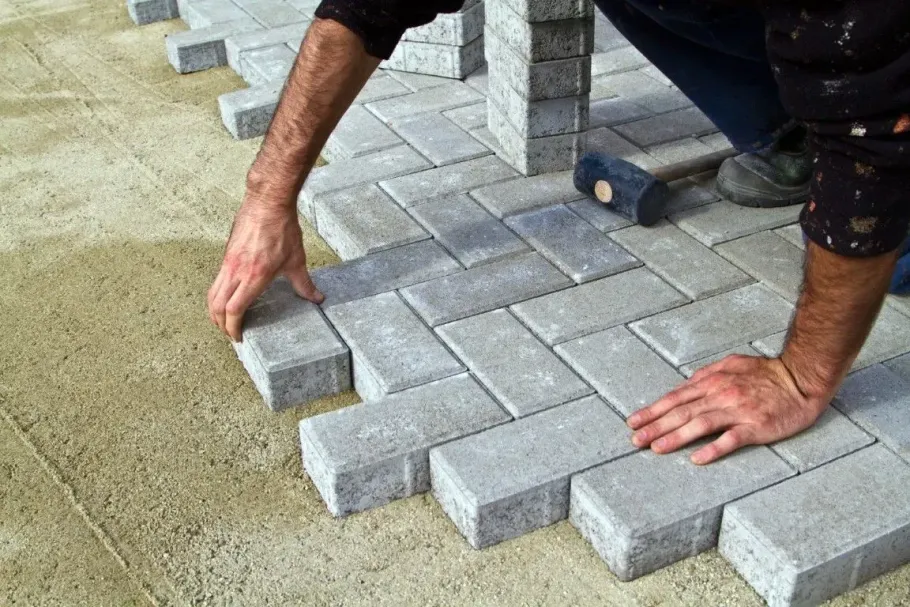 Worker laying gray paving stones on a sand base outdoors