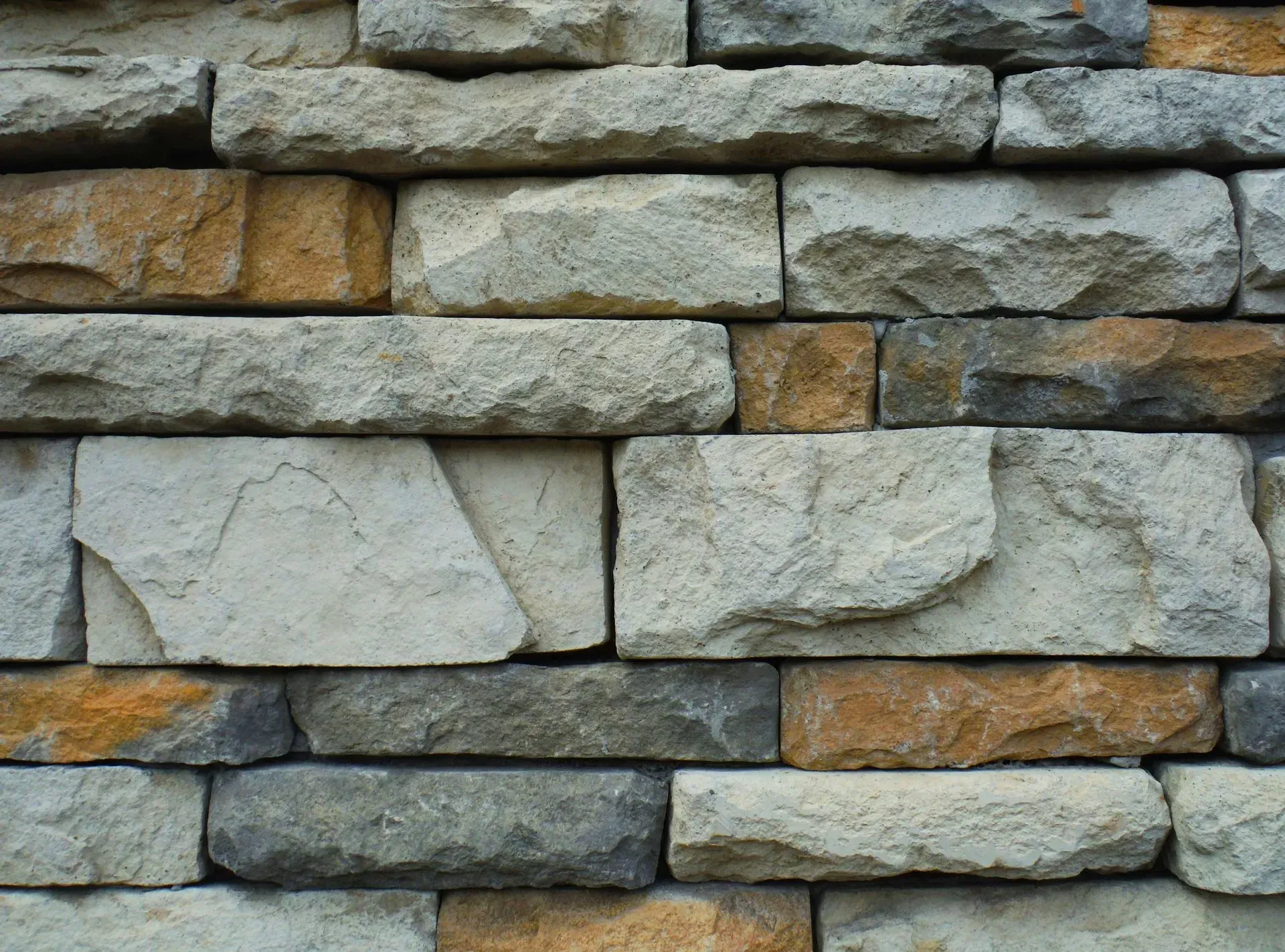 Gray and tan stacked stone wall with rough textured blocks