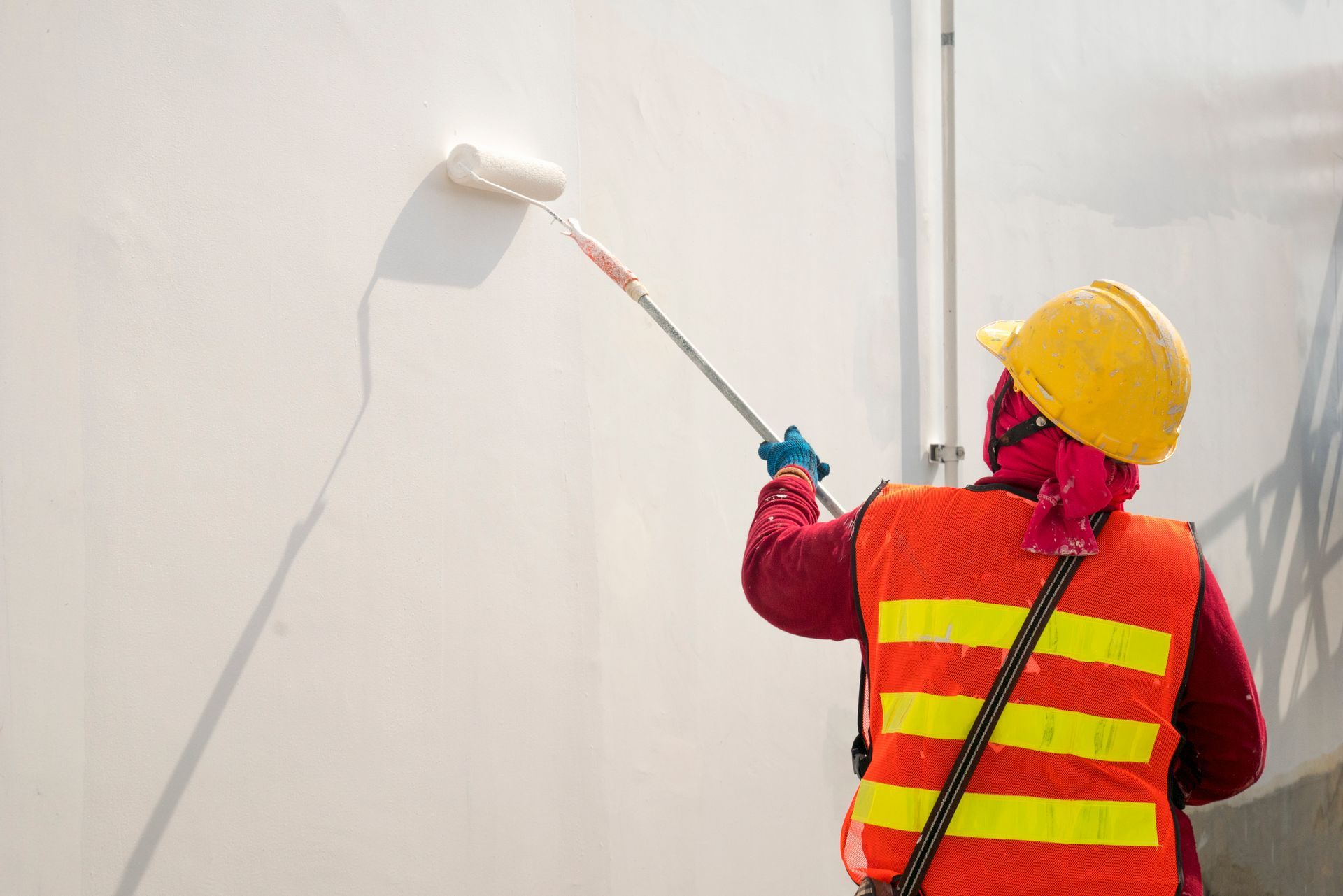 Construction worker wearing a hard hat and high-visibility vest painting a large exterior wall
