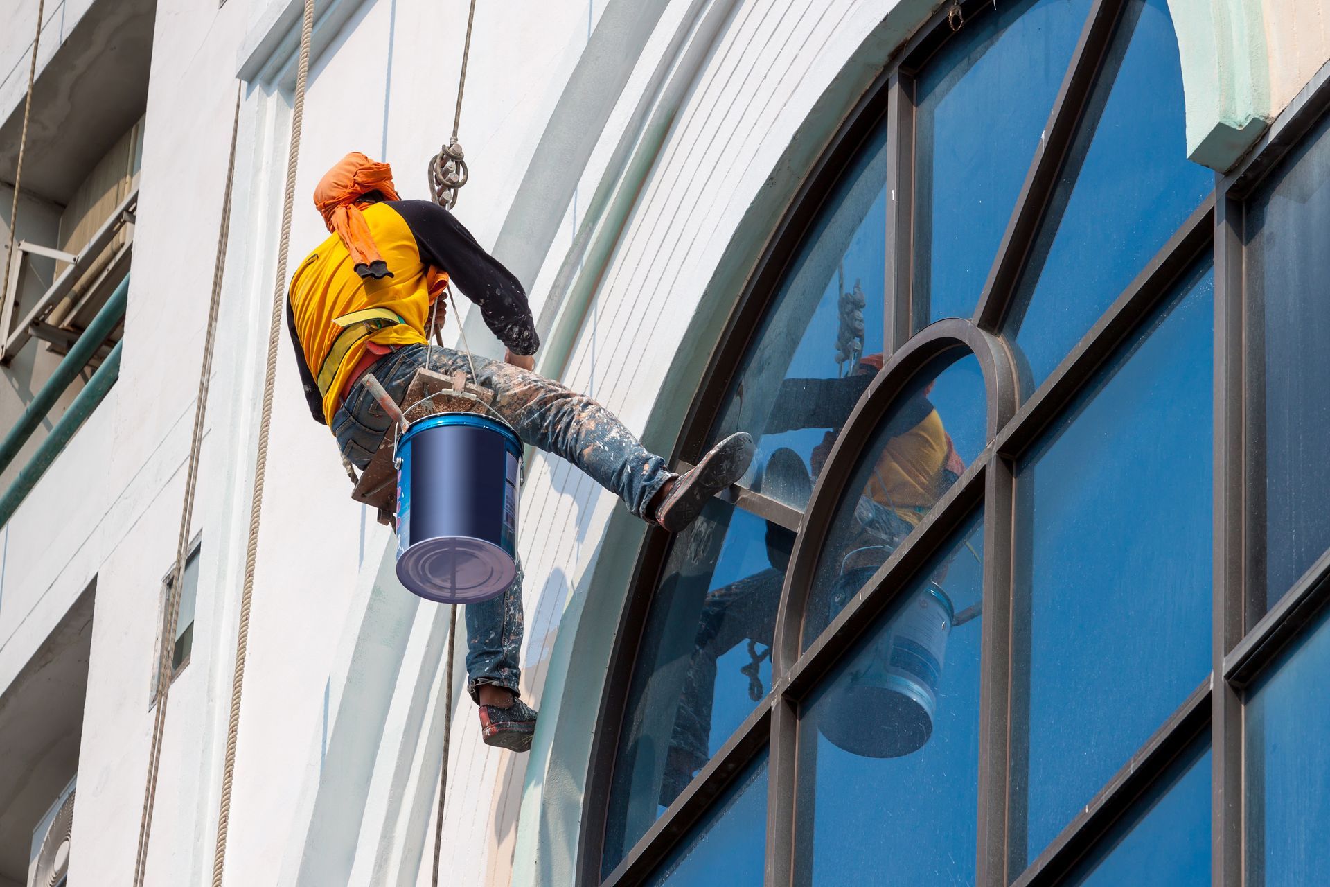 A man is painting the side of a building with a bucket.