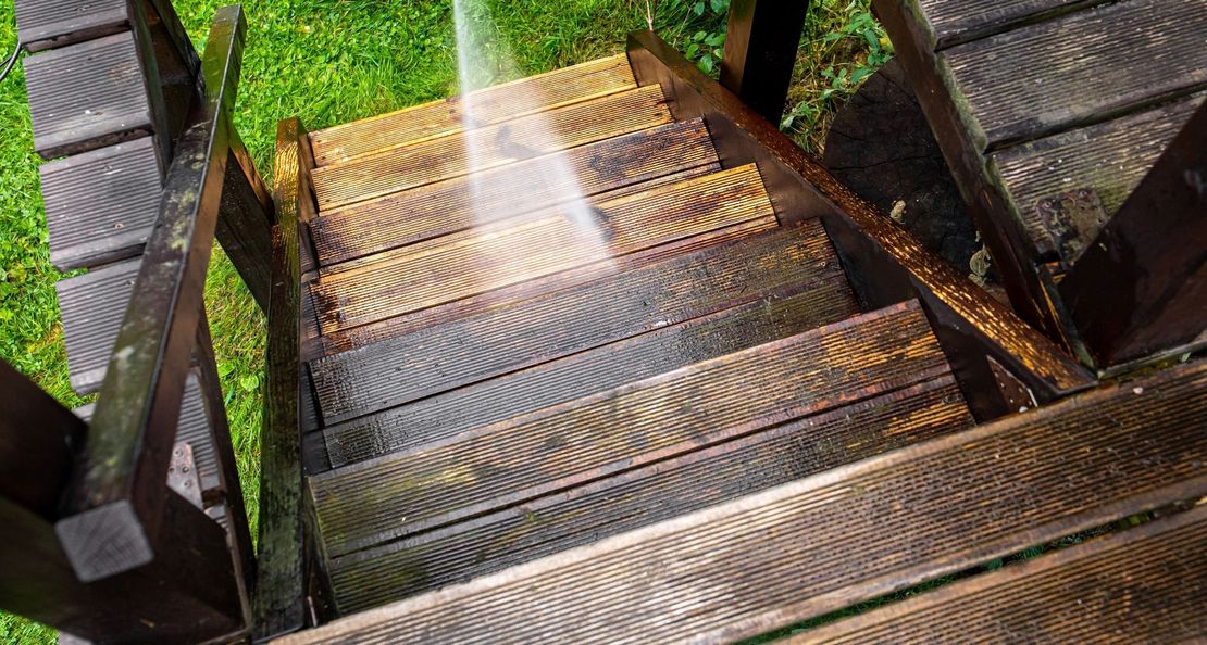 A person is cleaning wooden stairs with a high pressure washer.