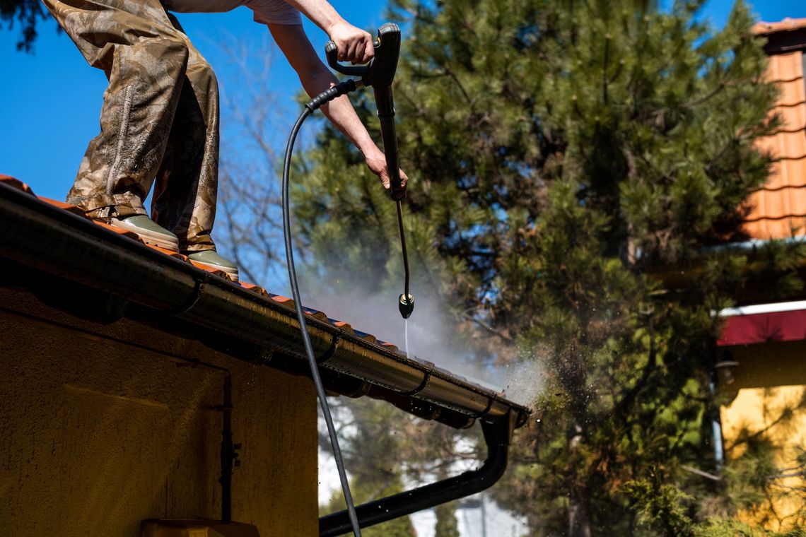 A man is cleaning the gutters of a house with a high pressure washer.