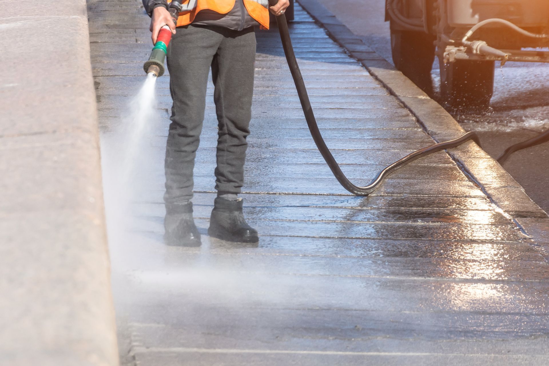 A man is cleaning the sidewalk with a high pressure washer.