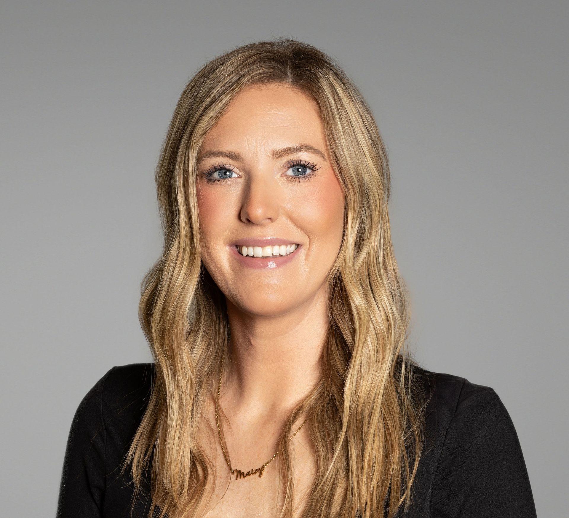 Blonde woman with a slight smile wearing a black top against a grey background.