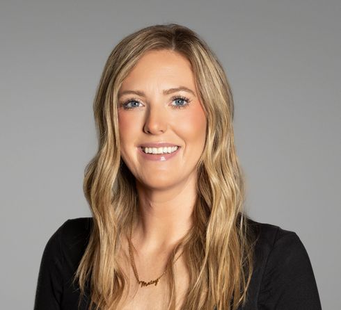 Blonde woman with a slight smile wearing a black top against a grey background.