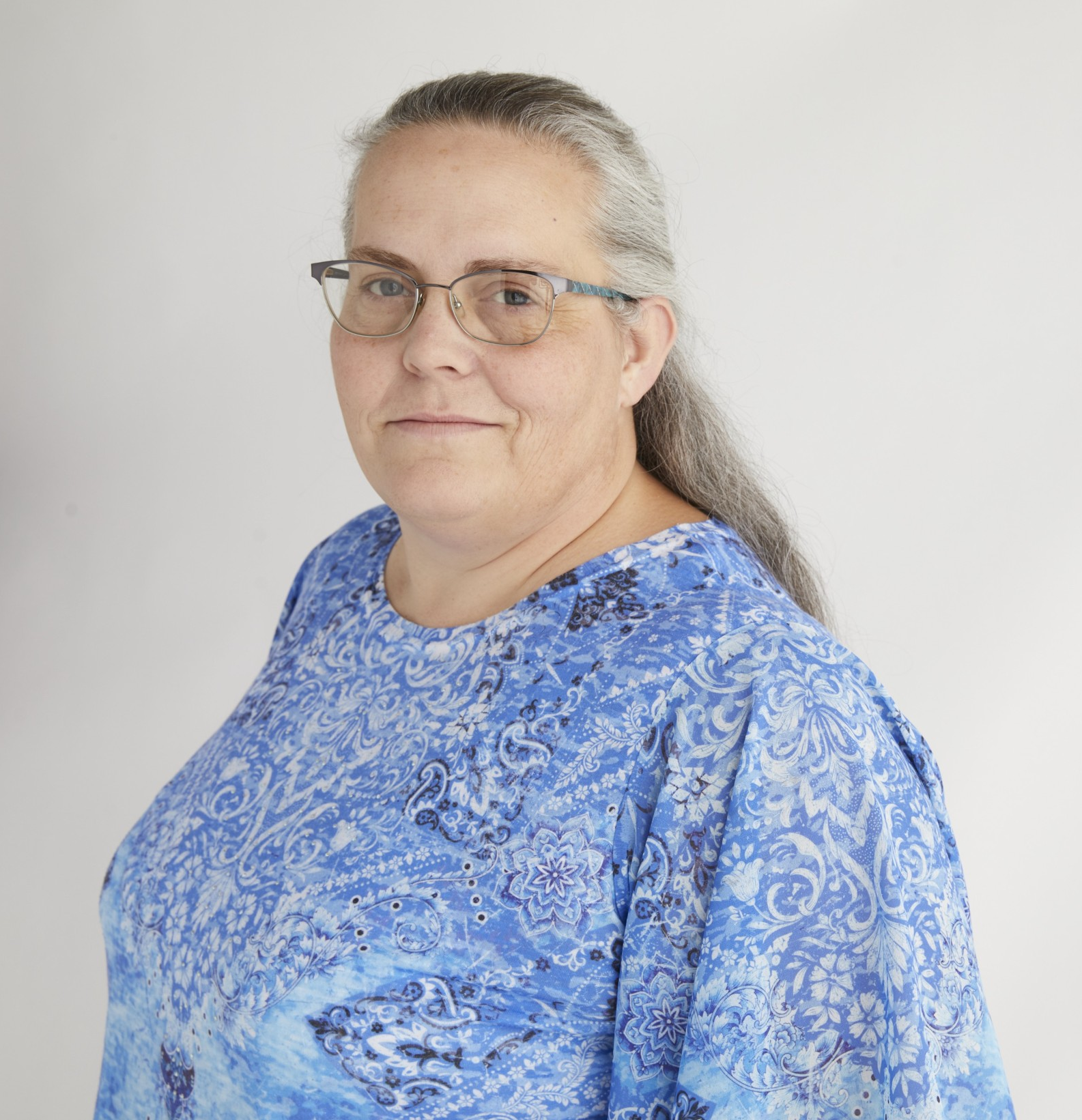 Woman with glasses wearing a blue patterned top, looking at the camera.