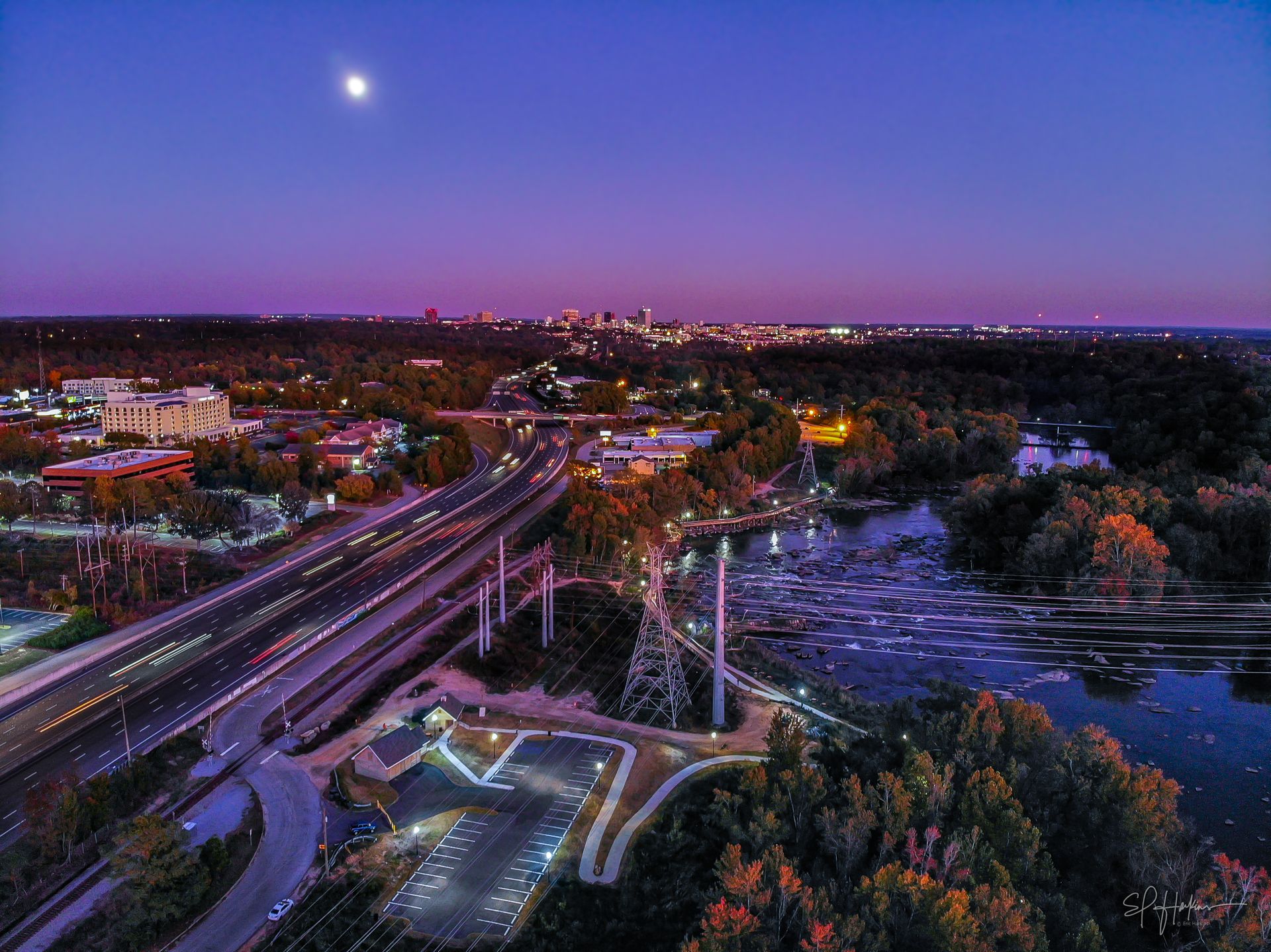 Woman in straw hat smiles, holding wine glass near a lake.