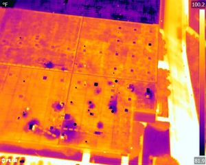 An aerial thermal infrared image showing varying heat patterns on a flat building roof, ranging from cool purple to hot red.