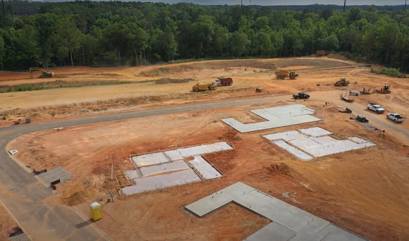 An aerial view of a construction site with several concrete building foundations laid out on orange earth.