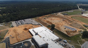 Aerial view of a school campus under construction with exposed dirt, foundations, and parking lots.