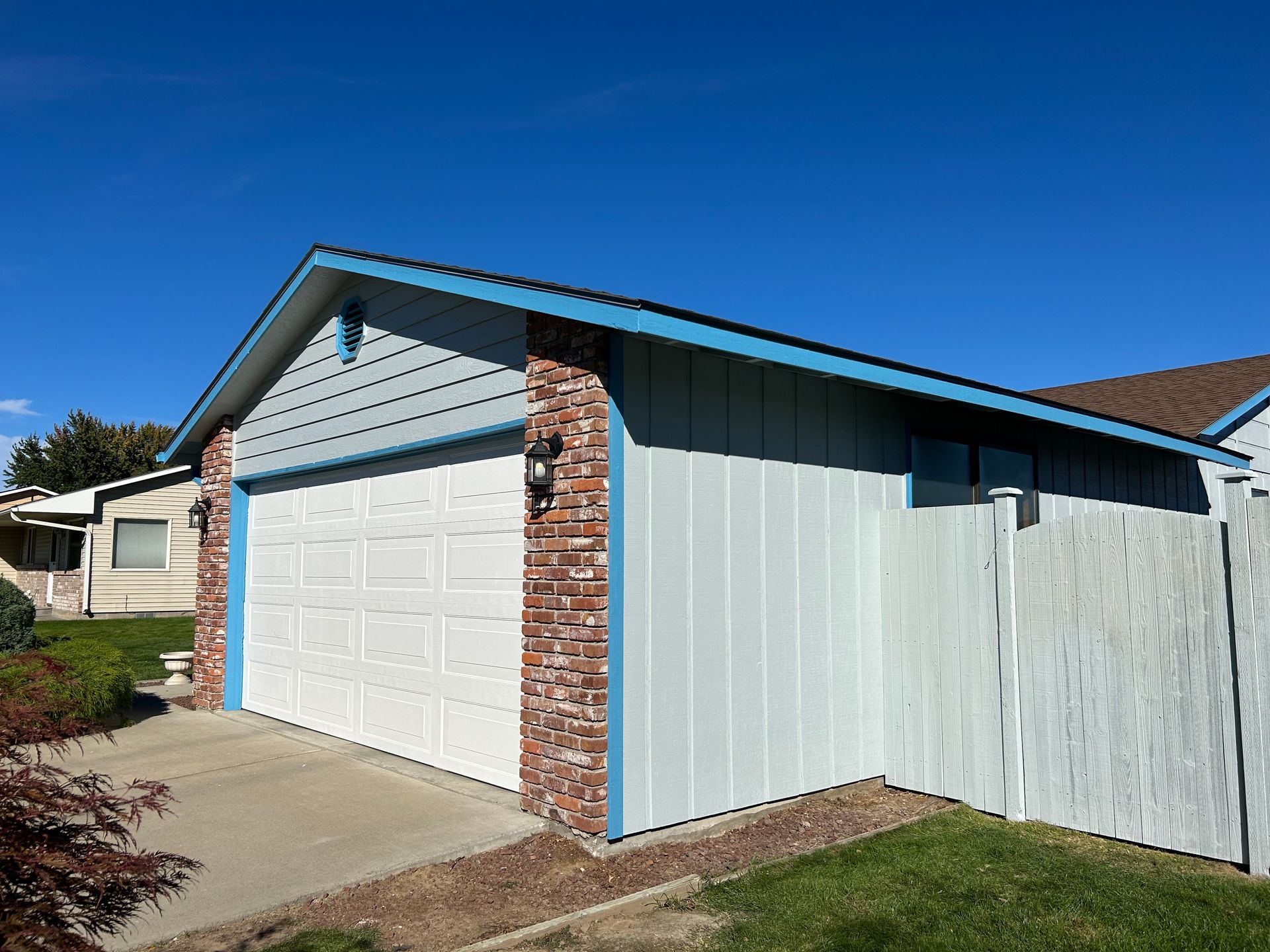 A white garage with a blue trim is next to a white fence.