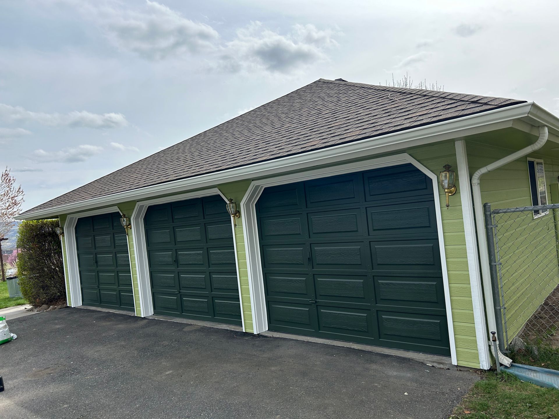 A green garage with three green garage doors and a gray roof.