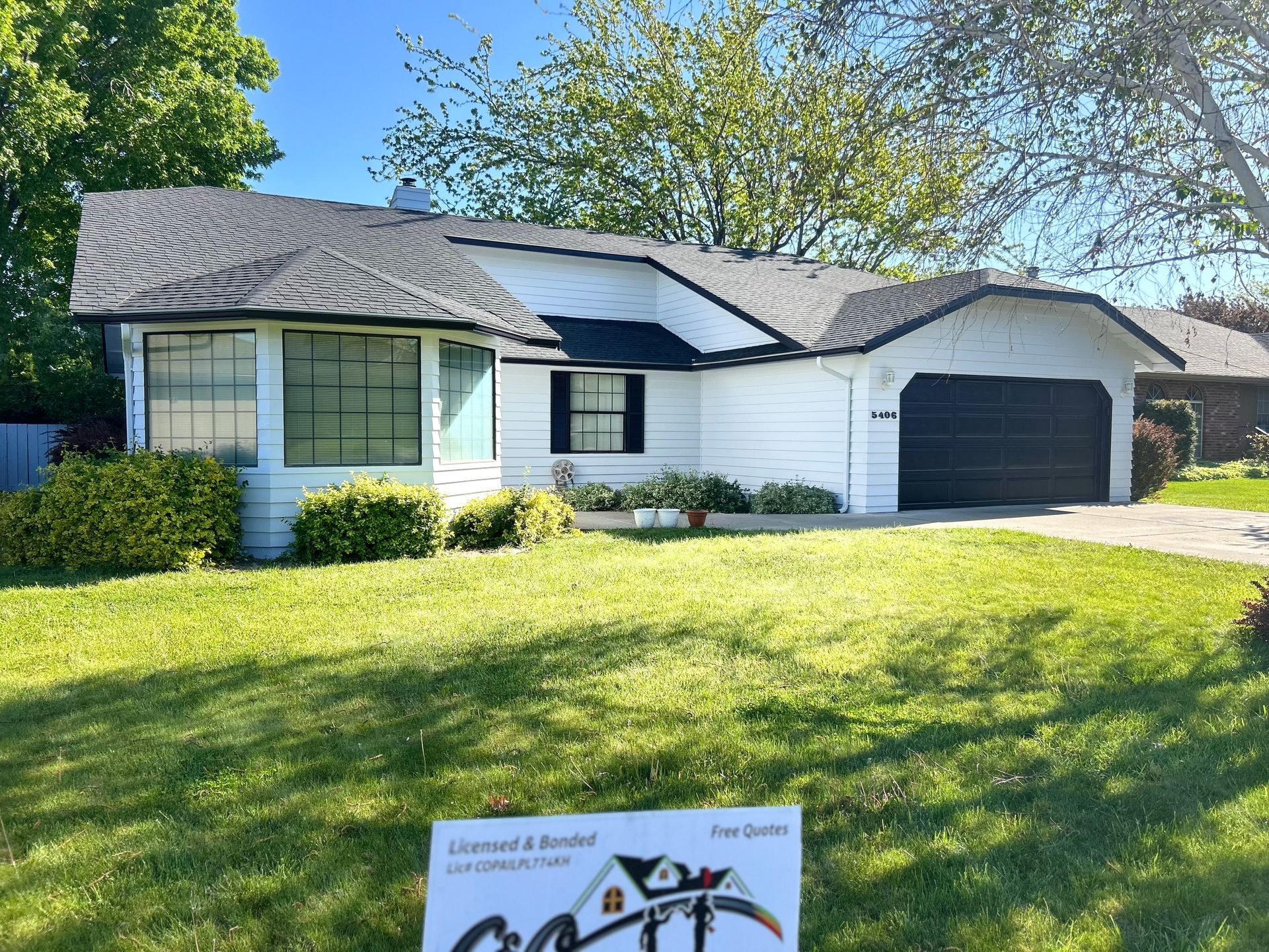 A white house with a black roof and a sign in front of it.