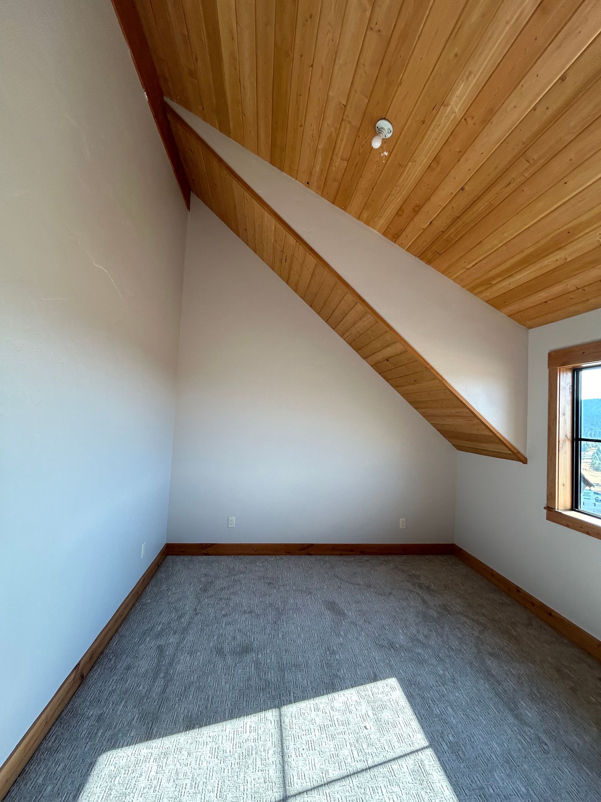 An empty room with a wooden ceiling and a window
