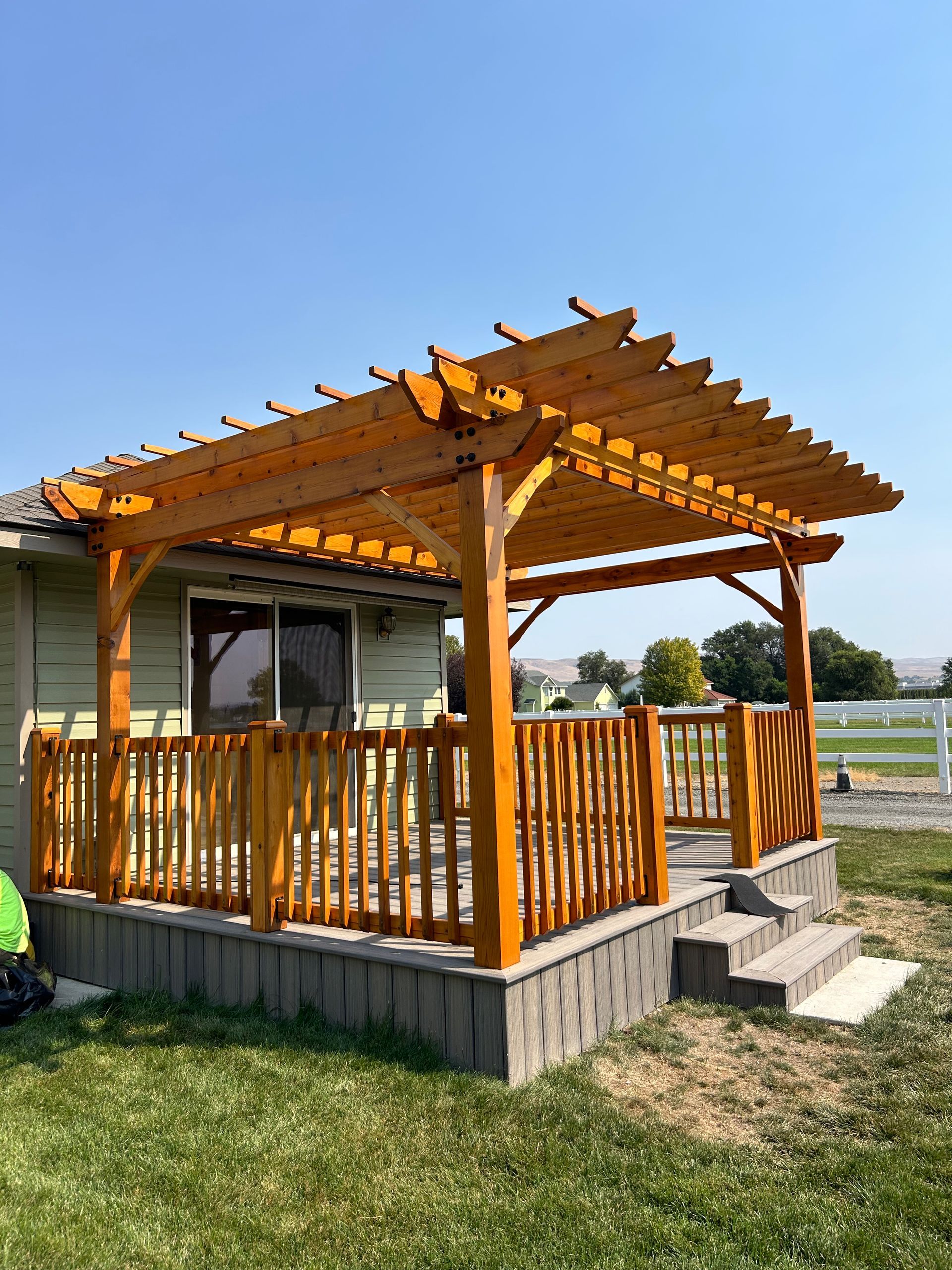 A wooden pergola is sitting on top of a deck next to a house.