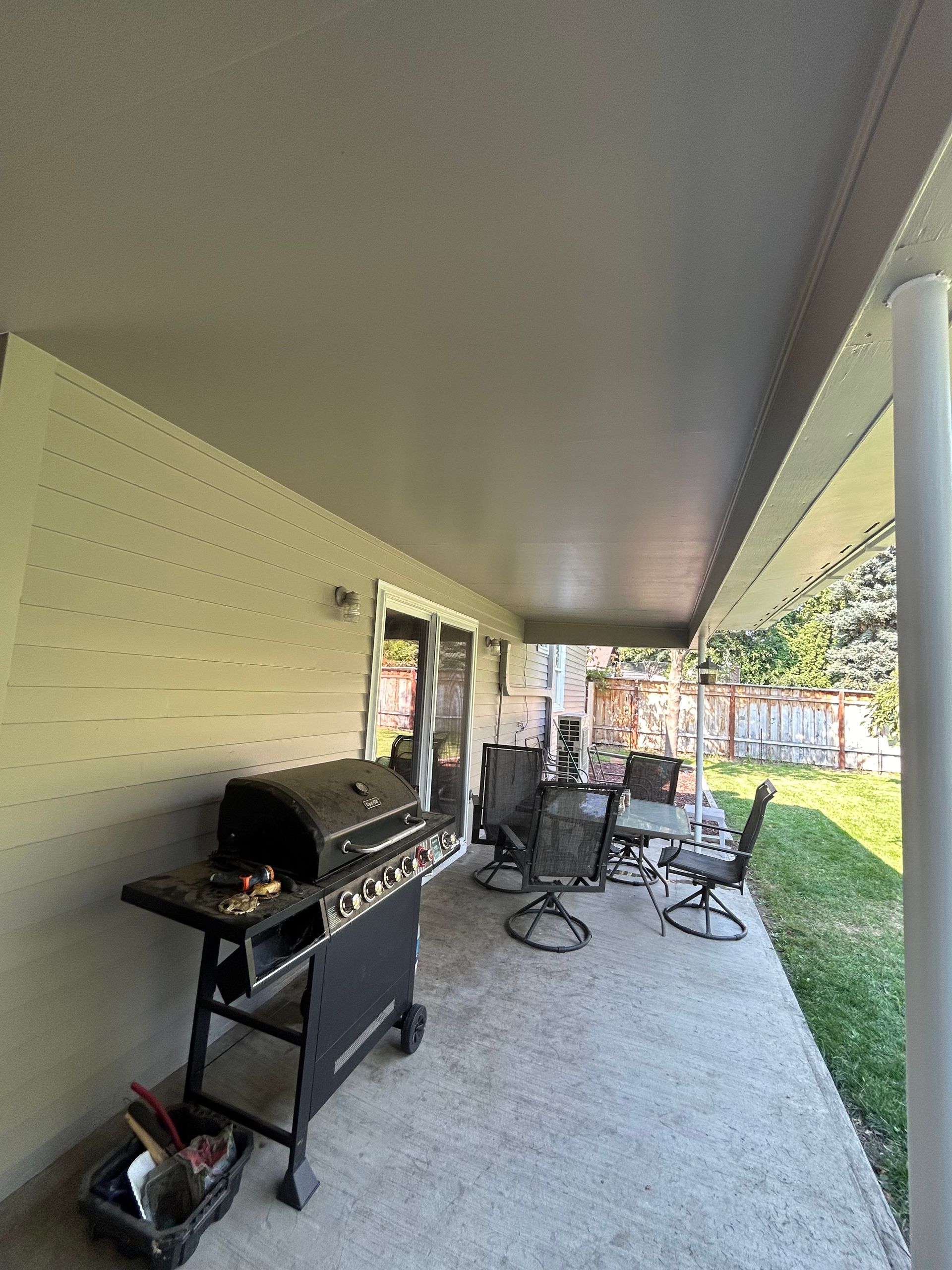 A porch with a grill , table and chairs on it.