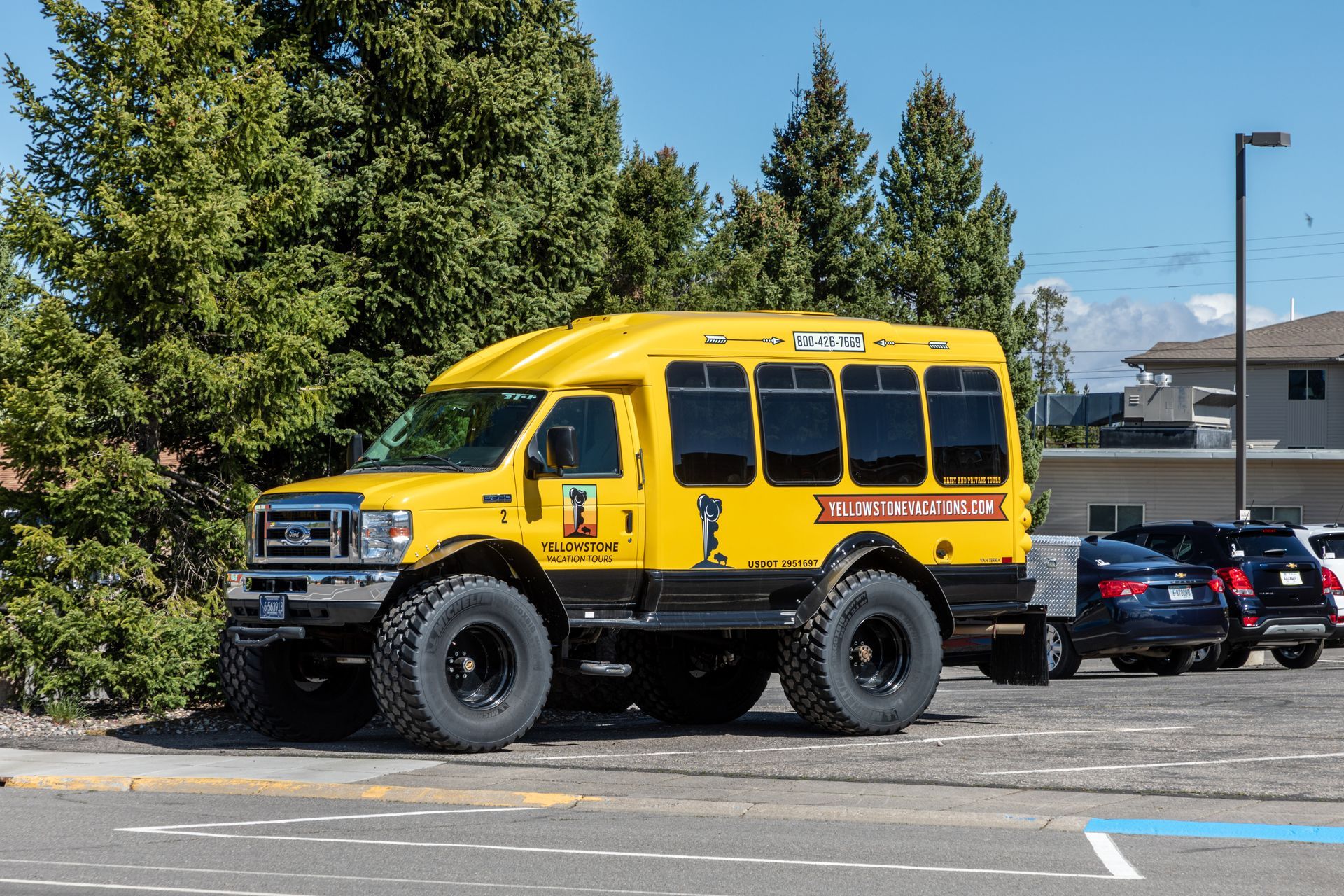 Yellow off-road truck parked in a lot beside trees and cars.