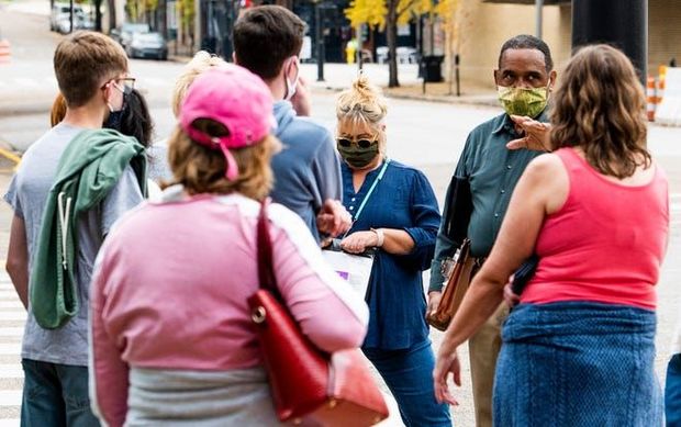 People wearing masks and casual clothes stand in a small outdoor group, talking on a sidewalk.