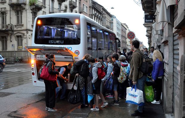 Crowded bus stop on a wet city street as people board an orange bus