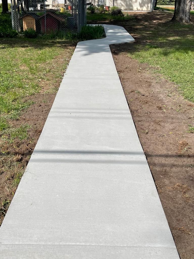 A long concrete walkway going through a grassy field.