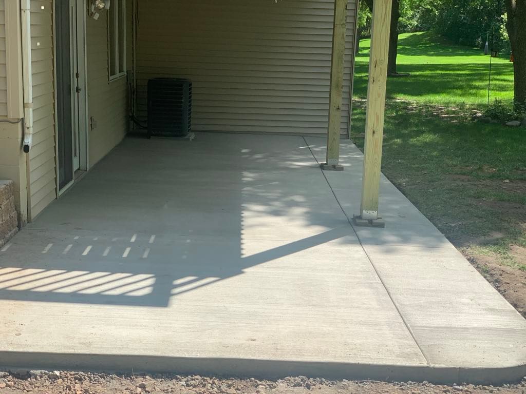 A concrete patio in front of a house with trees in the background