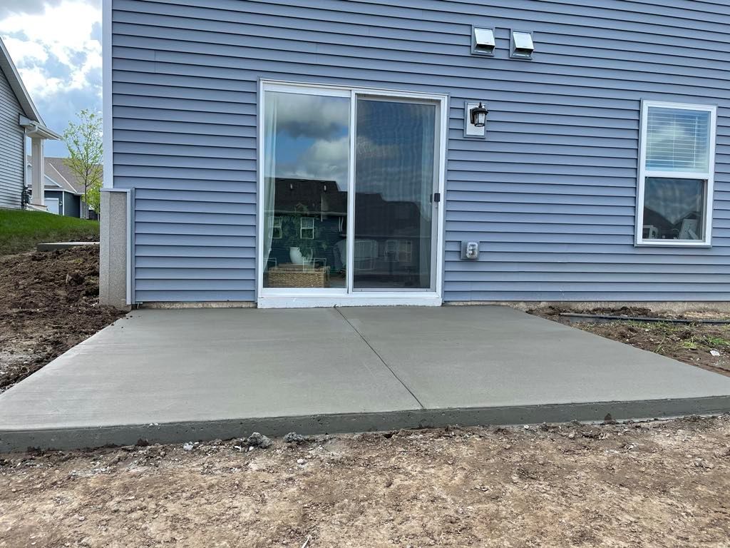 A concrete patio in front of a house with a sliding glass door.
