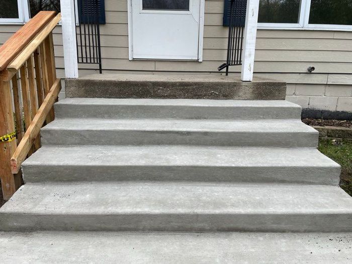 A set of concrete steps leading up to a house with a wooden railing.