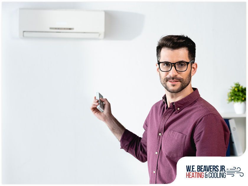 A man is holding a remote control in front of an air conditioner.
