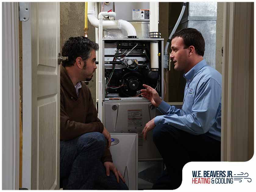 Two men are talking in front of a heating and cooling system