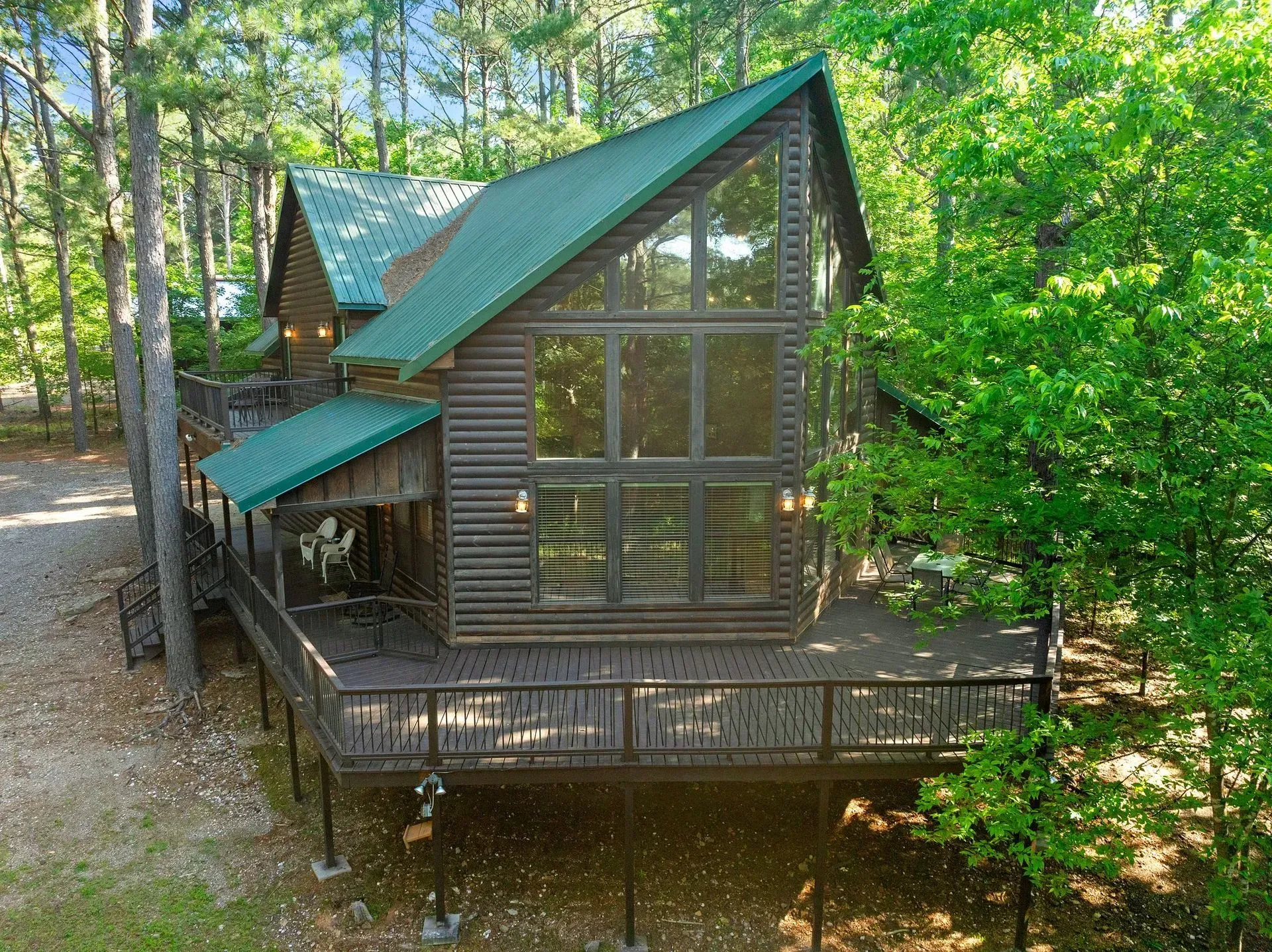 A rustic log cabin living area featuring a stone fireplace, leather furniture, and floor-to-ceiling windows with forest views.
