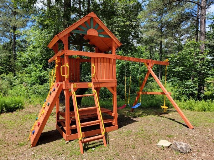A wooden playground set in the middle of a forest.
