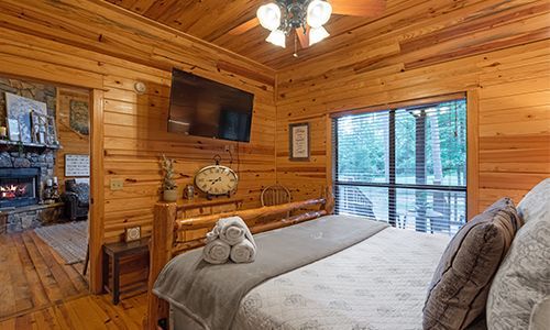 A bedroom in a log cabin with a king size bed , television and fireplace.
