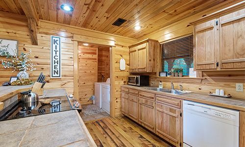 A kitchen in a log cabin with wooden cabinets and a dishwasher.
