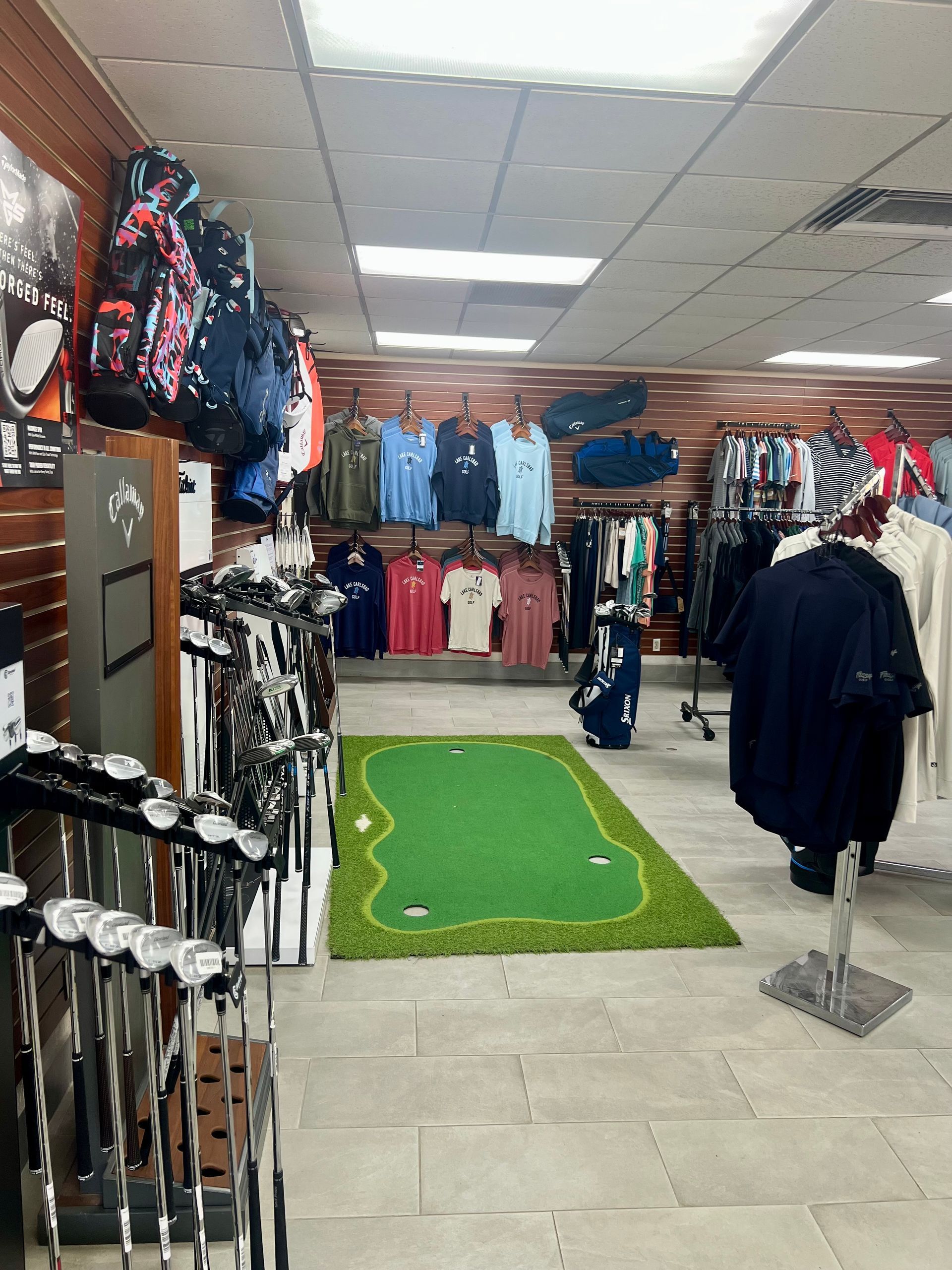 Golf equipment store interior, golf clubs on display, apparel, putting green, golf bags.