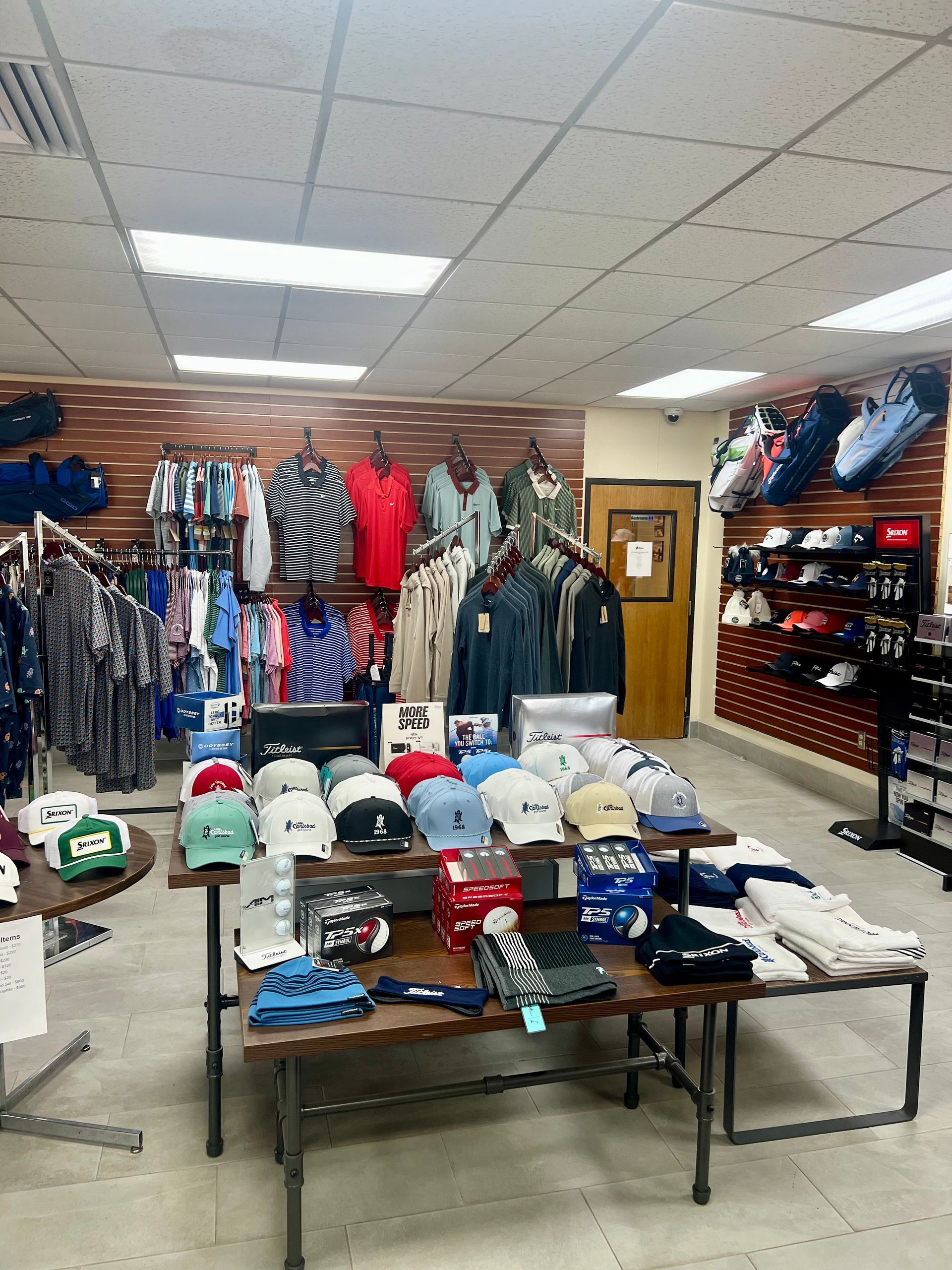 Clothing store interior, clothing and accessories displayed on racks and tables.